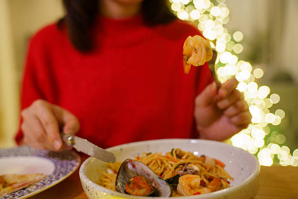 Hand holding slice of pizza during cozy Christmas dinner at home with candlelight and festive decorations. Warm holiday atmosphere, comfort food, casual home dining, and joyful seasonal lifestyle concept.