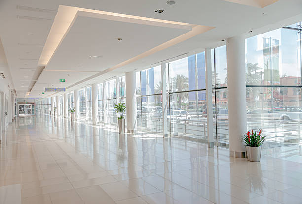 istock Bright empty corridor with floor to ceiling glass windows, white columns and potted palm plants in modern shopping mall interior with copy space 2253161423