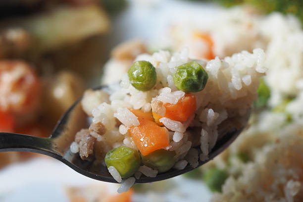 Spoonful of colorful vegetable rice featuring peas and carrots.