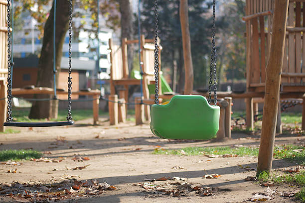 Children's swings are set in a playground filled with fallen leaves.