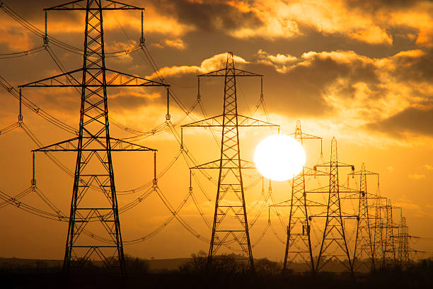 The sun sets behind electricity pylons crossing the landscape  at dusk. Long shot.