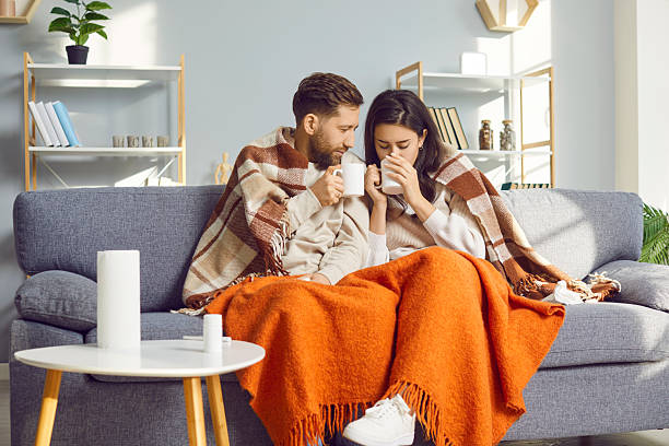 istock Young couple wrapped in blankets sitting on sofa at home 2253165107