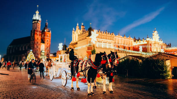Krakow’s Main Market Square is captured at night with St. Mary’s Basilica and the Cloth Hall illuminated by festive Christmas lights, while crowds of people stroll between market stalls and decorations. The wet cobblestone street, blurred motion of pedestrians and cyclists, and glowing historic architecture create a vibrant winter holiday atmosphere ideal for themes of tourism, Christmas markets, and European city breaks.