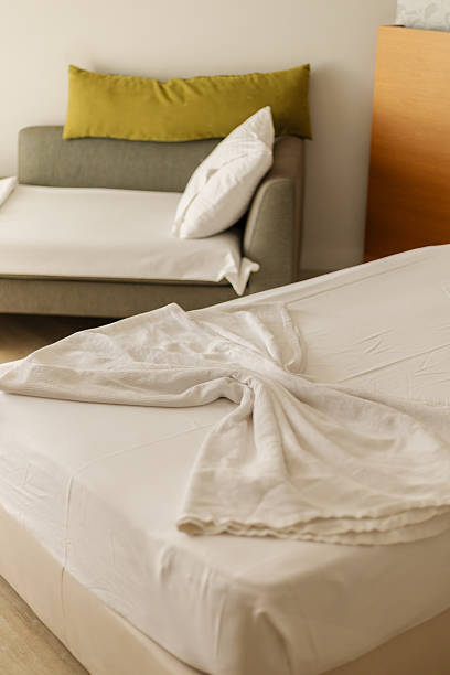 istock A room shows a made bed with white sheets and a neatly arranged sofa. Sunlight fills the space, indicating daytime. The setting is ready for guests 2253172646