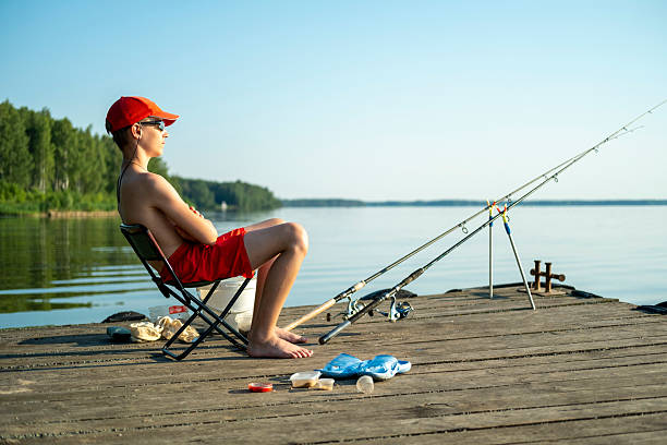 Boy sitting on a curved white wooden bridge and touching the railing with a stick, exploring details with curiosity. Concept of childhood discovery, outdoor learning and natural lifestyle.