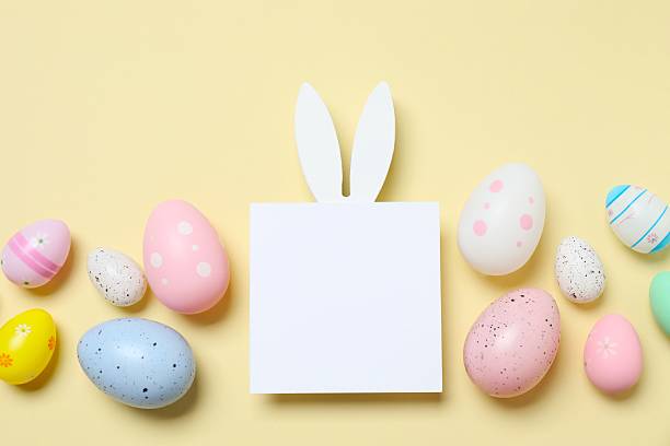 istock Happy Easter. Colorful eggs with bunny ears and white paper card on color background, space for text or advertising 2253180708
