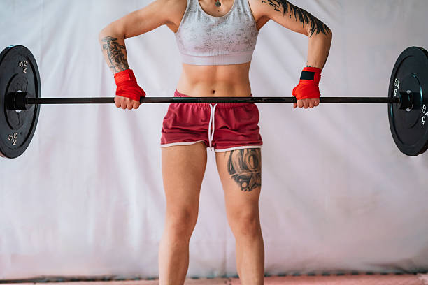 Strong mid-30s woman lifting heavy barbell in home gym, showcasing power, muscle, focus and dedication to fitness training