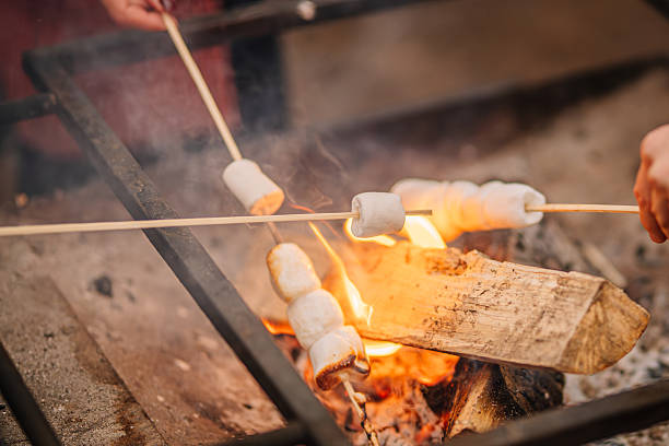 istock Group of hands roasting marshmallows over an open fire, with glowing flames and smoke creating a warm atmosphere, perfect for outdoor gatherings and camping experiences 2253184540