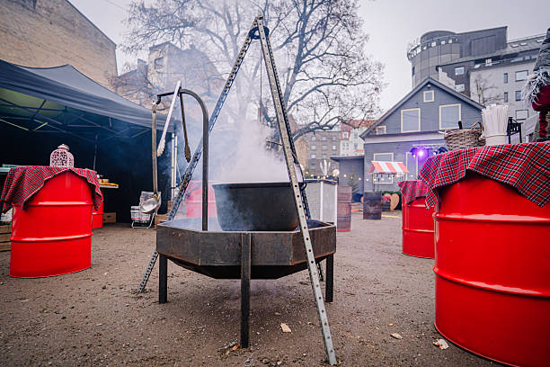 istock Large black cauldron suspended over a fire pit, surrounded by red barrels and festive decorations, creating a warm atmosphere for outdoor gatherings and celebrations 2253184875