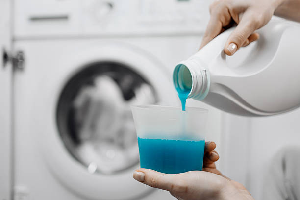 istock Person pours blue liquid detergent into a measuring cup in a laundry room 2253185503