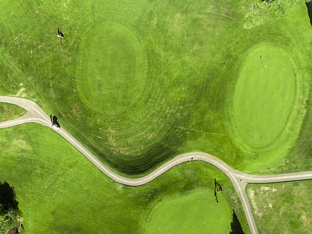 Aerial view of a lush green golf course with golfers navigating winding fairways and a golf cart, showcasing the harmony of sport and scenic landscape.