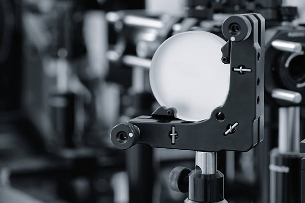 Optical equipment including telescope and lenses are displayed on a table in a laboratory. Optics and photonics concept science experiment with laser background