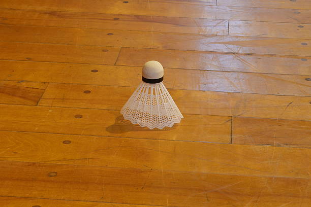 A white badminton racket is sitting on a wooden floor. The racket is the only object in the image