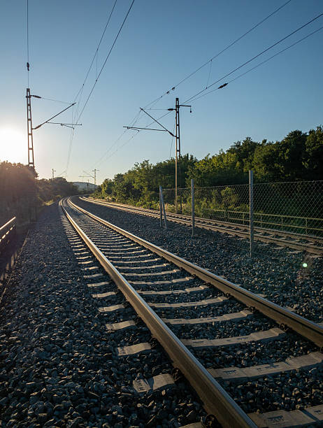 istock sunlit railway tracks with electric lines in forest 2253192436