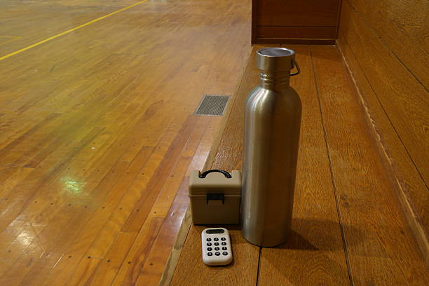 A silver water bottle sits on a wooden floor next to a remote control. The scene is simple and uncluttered, with the focus on the water bottle and remote. Scene is calm and relaxed