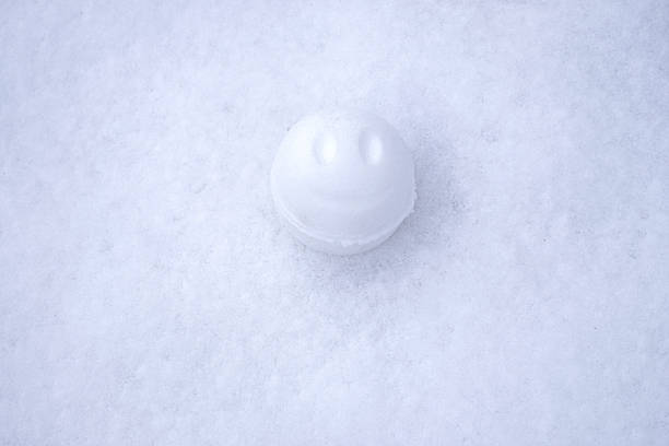 A cheerful snow ball with smiley face on in the middle of clean white snowy surface. A playful winter photograph perfect for festive and joyful content, celebrate the winter, perfect for winter fun themes, desktop wallpapers etc.