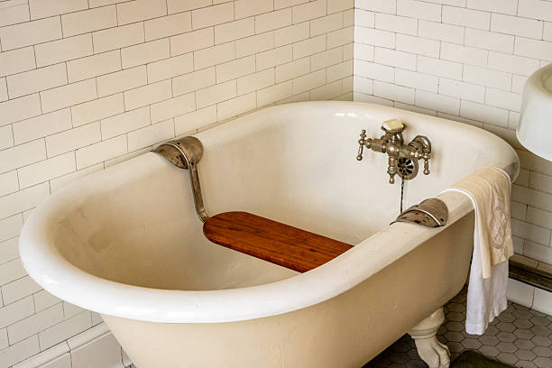 Stock photo showing luxury bathroom suite with Victorian style white ceramic, freestanding, curved roll top bath with claw feet, chrome, wall mounted bath mixer tap and stone tiled wall and flooring.