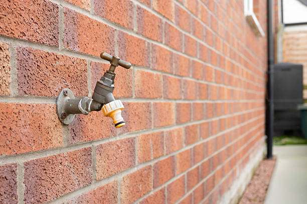 Close up of an outdoor garden tap with hose connector mounted on a brick wall beside a house. Concept of water supply, gardening, home exterior, and household maintenance