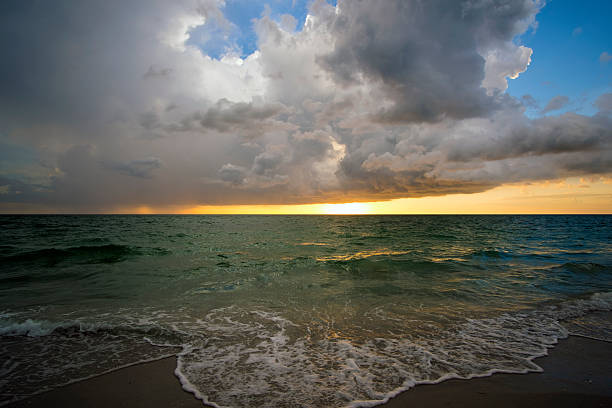 Ocean landscape with thunderstorm clouds over rough evening sea water waves crushing on sandy beach. Beautiful seascape at sunset.