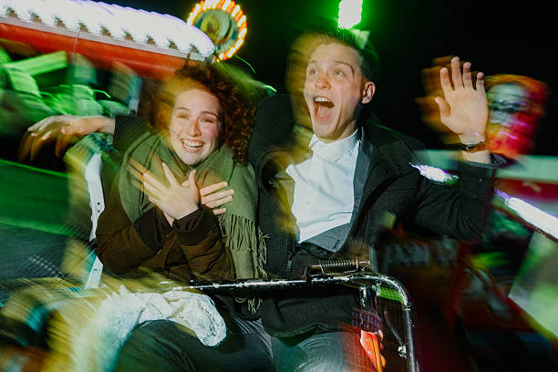 Young couple screaming with excitement and joy while experiencing a fast thrill ride at a vibrant fairground at night