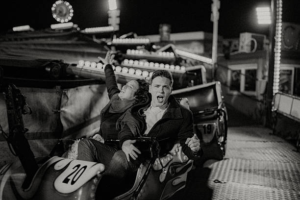 Young couple screaming with joy on a thrilling fairground ride at night, lights blurring as they share an excited, carefree moment