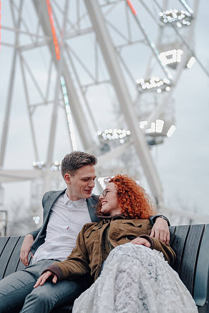 istock Happy couple relaxing on bench by ferris wheel 2253203504