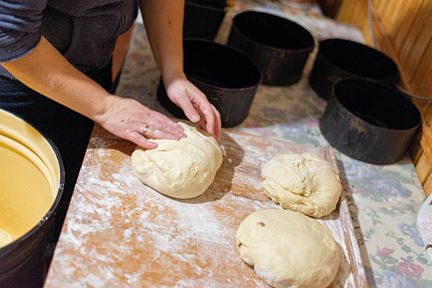 Close-up of female hands shaping bread dough in a rustic home kitchen. Homemade baking process with black baking forms on the table. Traditional cooking of bread from scratch.