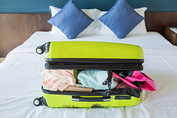 istock Overpacked green suitcase on hotel bed with clothes spilling out 2253205581