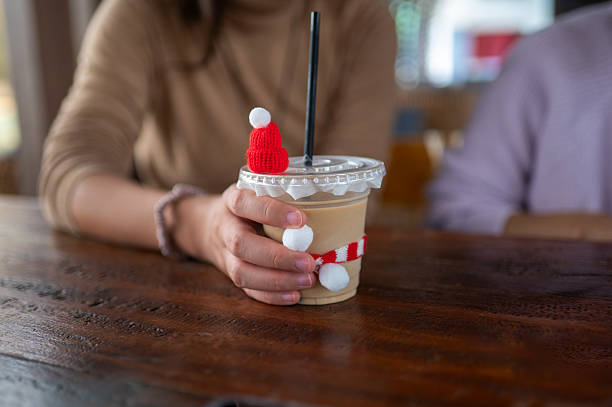 A delightful scene showing a person's hand holding a Christmas vibes decorative coffee  with a Santa hat and playful decorations, encapsulating the spirit of celebration and joy in winter festivities.