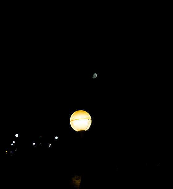 The image shows the contrast between an illuminated spherical street light and a crescent moon in a dark night sky.