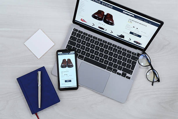 istock Online store website on laptop screen. Computer, smartphone, stationery and glasses on light grey wooden table, flat lay 2253211809