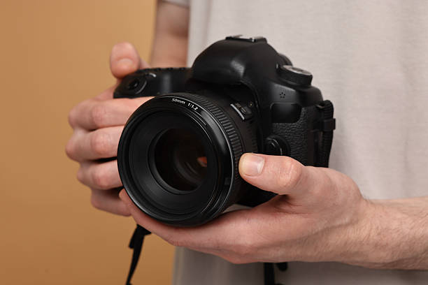 istock Photographer holding camera on beige background, closeup 2253212370