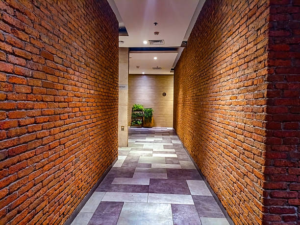 Hallway interior featuring textured brick walls and a tiled floor, leading to an open area with plants, creating a modern architectural space with a blend of rustic and contemporary design.