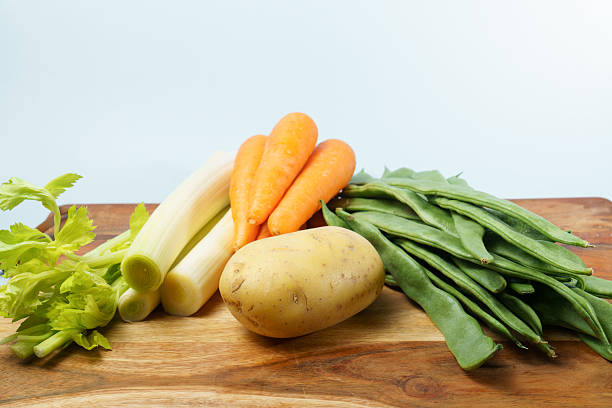 Fresh vegetables including potato, carrots, leeks, green beans, and celery ready on a chopping board for cooking