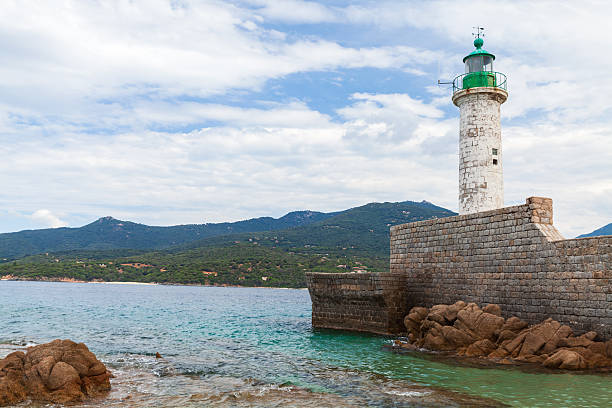 A sturdy stone breakwater supports a classic lighthouse tower. Coastal landscape of Propriano, Corsica, France