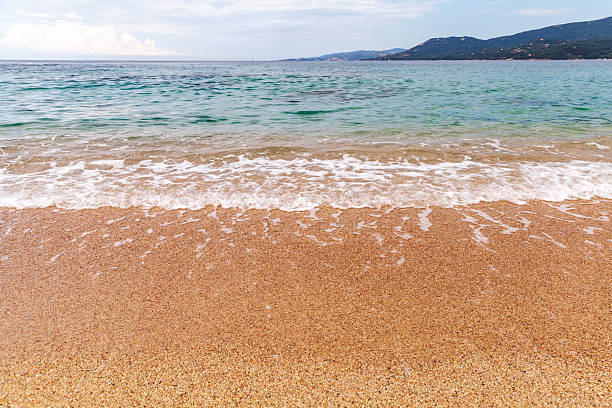 Shore water covers sandy beach of Propriano under blue sky on a summer day. Coastal landscape. Corsica, France