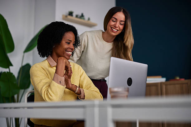 istock Two women collaborate at a bright office desk, smiling at a computer screen during a friendly work session 2253216604