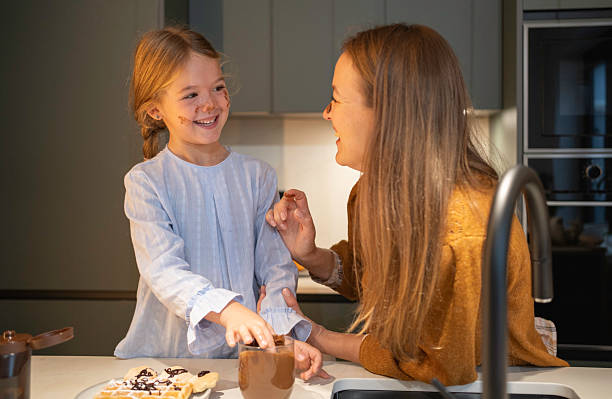 Mother and daughter smiling, eating dessert, enjoying family time in the kitchen