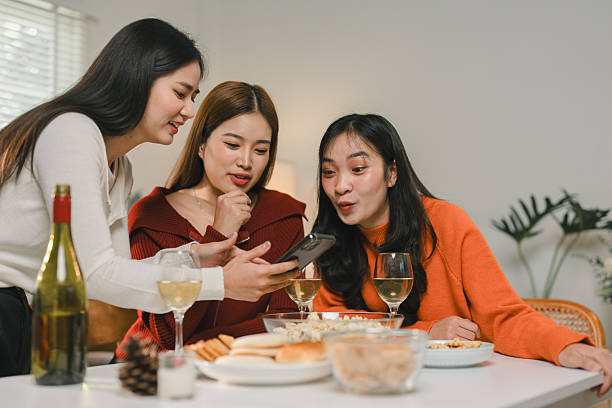 istock Three women gather around a table, enjoying wine and snacks while sharing moments on a smartphone. The warm atmosphere suggests a casual and joyful social gathering 2253225085