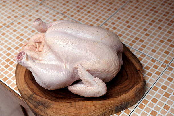 A pile of raw chicken drumsticks is on display at a market stall, ready for sale.