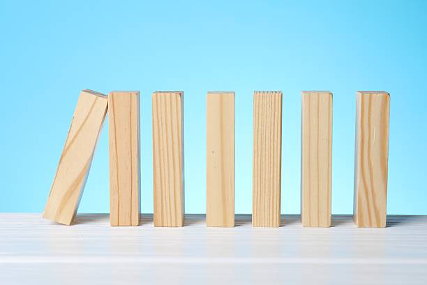 istock Risk. Wooden blocks falling on white table against light blue background 2253226011