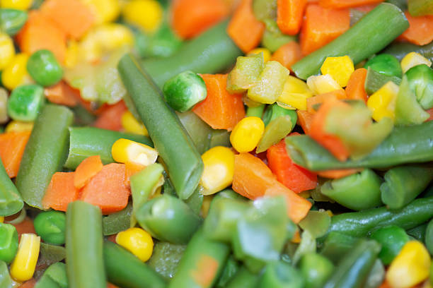 Homemade sautéed green beans with bacon bits and lemon zest sits on a table full of food.