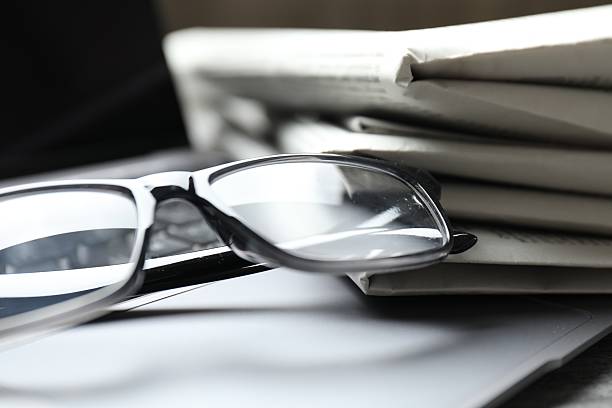 istock Stack of newspapers, laptop and glasses on table, closeup 2253226976