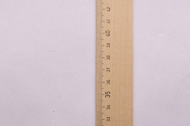 A ruler is shown with the numbers 0 through 5 on it. The ruler is placed on a piece of wood, and the numbers are clearly visible