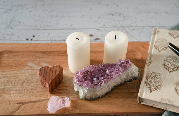 A peaceful composition of unlit white candles, amethyst and rose quartz crystals, a decorative journal with a pen, and a wooden heart on a rustic tray. This cozy scene evokes mindfulness and intention-setting for a calm start to the year. Generous copy space available.