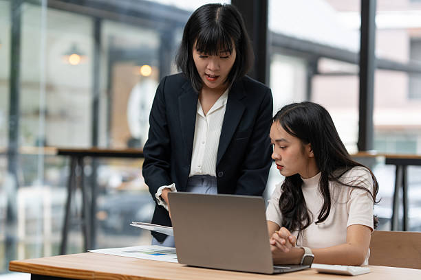 istock Two asian businesswomen engaging in a productive discussion about their work, utilizing a laptop and reviewing documents in a sleek, modern office environment 2253228543