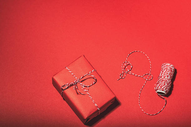 Christmas background, postcard. Red gift box and striped twine on a red background