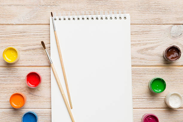 istock Album pages and paints, pencils, brush on a colored background. Top view with empty space. workplace for creativity. home teaching concept drawing 2253230675
