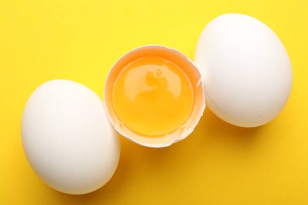 istock Whole and broken chicken eggs on yellow background, above view 2253238809