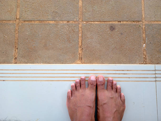 Feet standing on a tiled floor with a white mat.